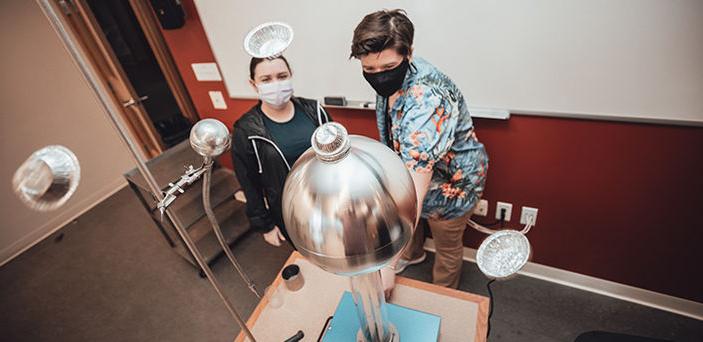 2 BSU students operating an electro magnetic tower with small foil pie plates on the top and flying in the air around it